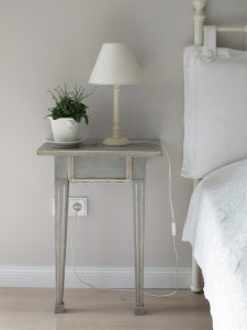 distressed shabby chic bedside table with small white lamp and plant on