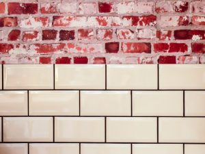 cream tiles with black grout against red brick wall.