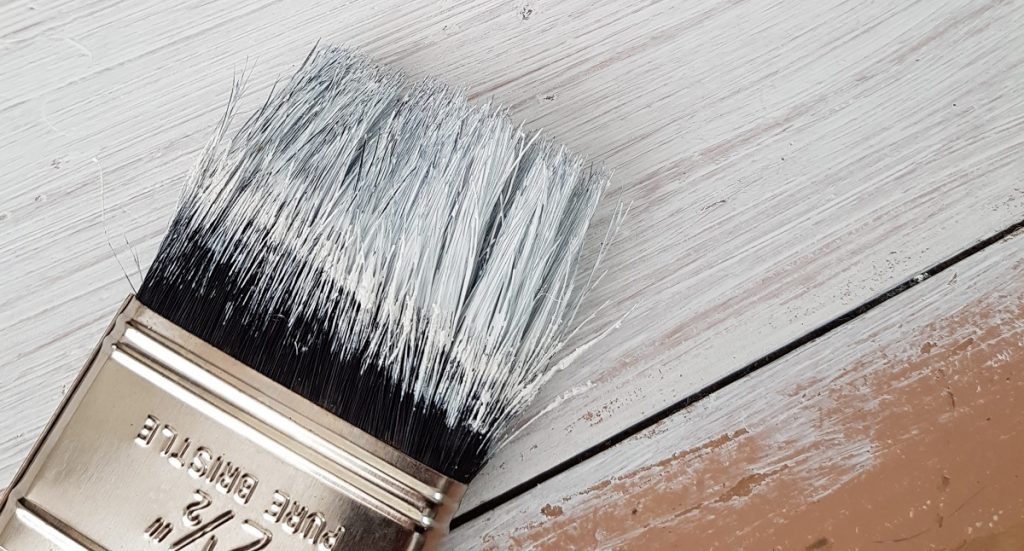 A paint brush being used to paint a hardwood floor.